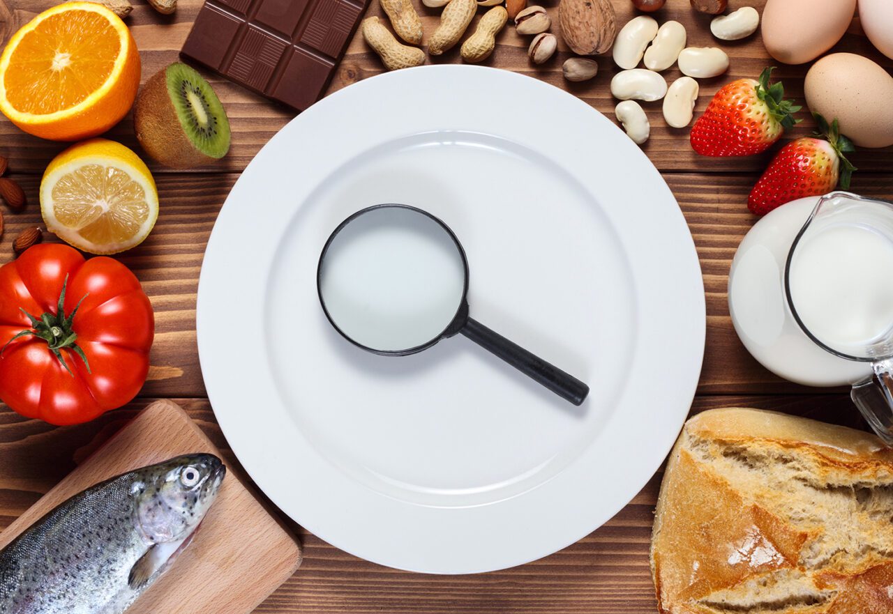 Allergy food concept. Food and empty plate with magnifier on wooden table.
